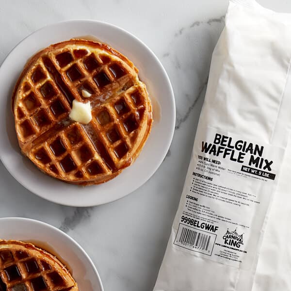 Two waffles on a plate with syrup and butter next to a bag of Carnival King Belgian Waffle Mix.