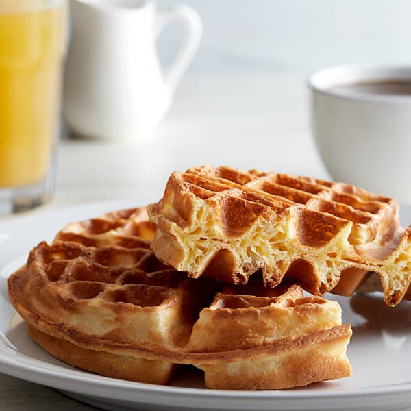A plate with Carnival King Belgian waffles next to a cup of coffee and a pitcher of liquid.