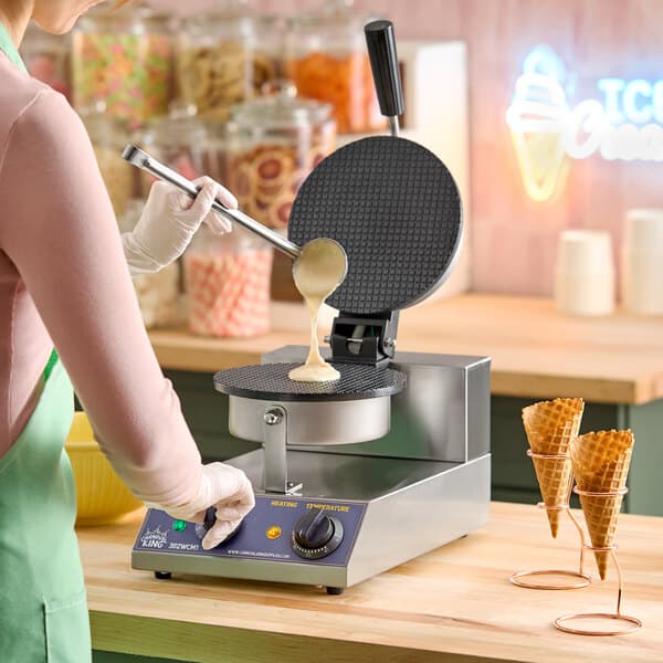 A stainless steel Carnival King WCM1 8-inch non-stick waffle cone maker being used to pour batter onto the cooking surface.