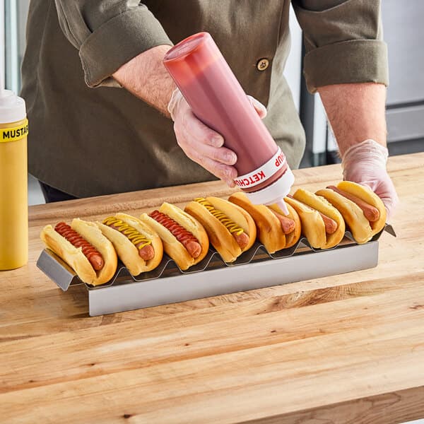 A man using a Carnival King stainless steel hot dog preparation tray to put ketchup and mustard on hot dogs.