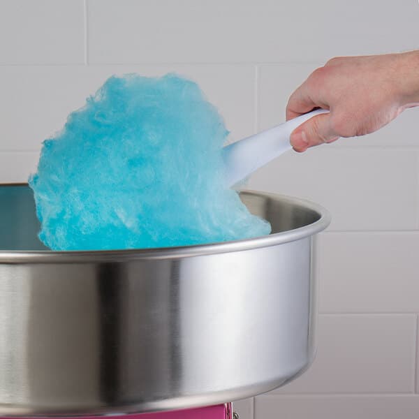 A hand holding a white cotton candy cone with blue cotton candy above a metal cotton candy machine.