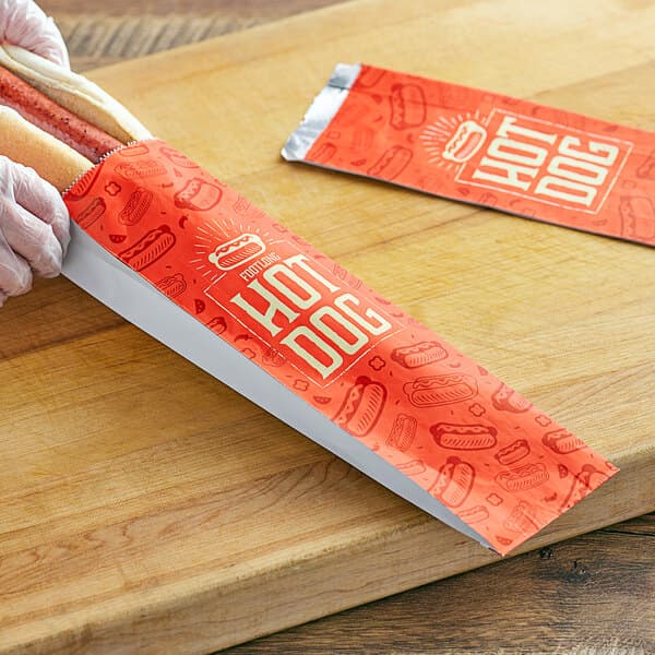 A person holding a Carnival King footlong hot dog in a red foil bag with white text.