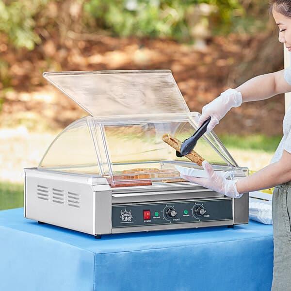 A woman putting a hot dog on a Carnival King hot dog roller.