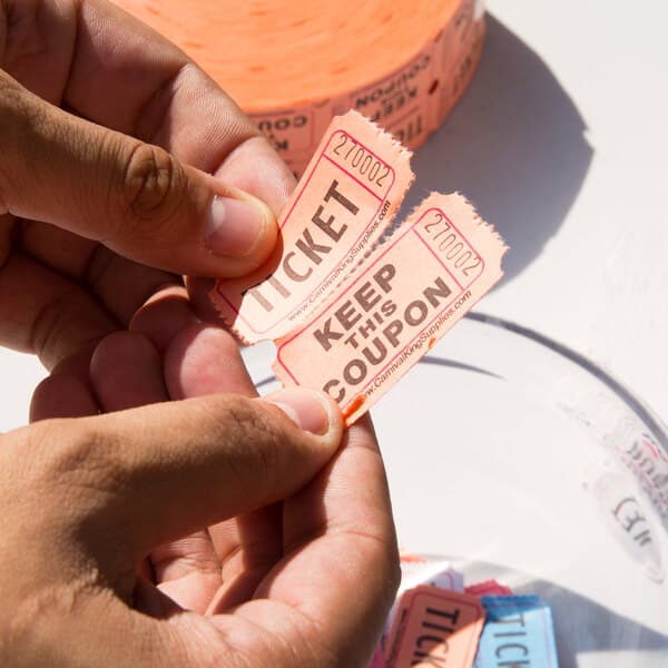A person holding two Carnival King orange raffle tickets.