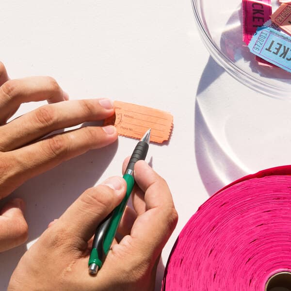 A person writing on a Carnival King orange raffle ticket on a table in a stadium concession stand.