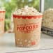 A close up of a Carnival King 130 oz. popcorn bucket on a table with two boxes of popcorn with red text.