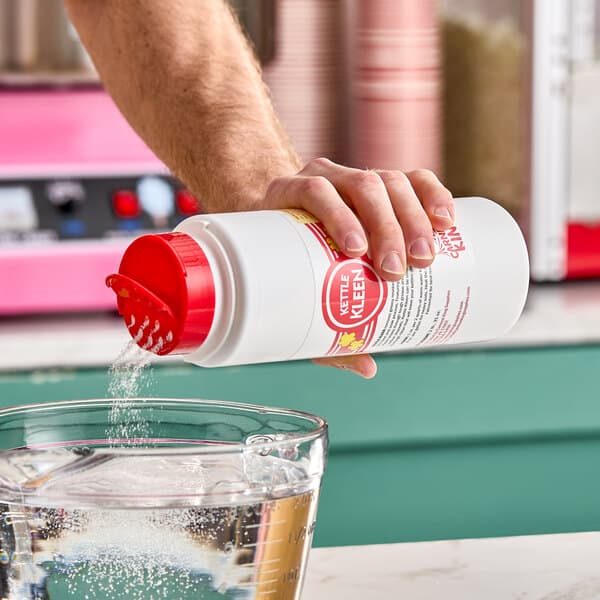 A container of Carnival King 31 oz. Kettle Kleen Concentrated Kettle Cleaner being poured into a glass measuring cup of water.