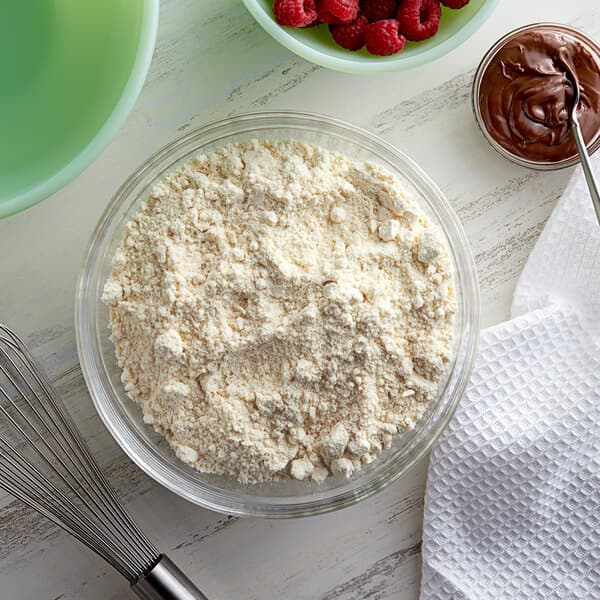 A bowl of flour and a whisk next to a bowl of chocolate spread.