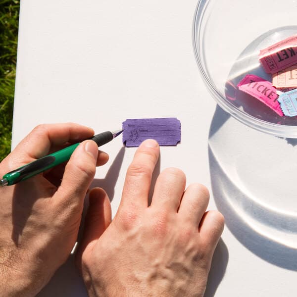 A person writing on a Carnival King purple raffle ticket on a table.