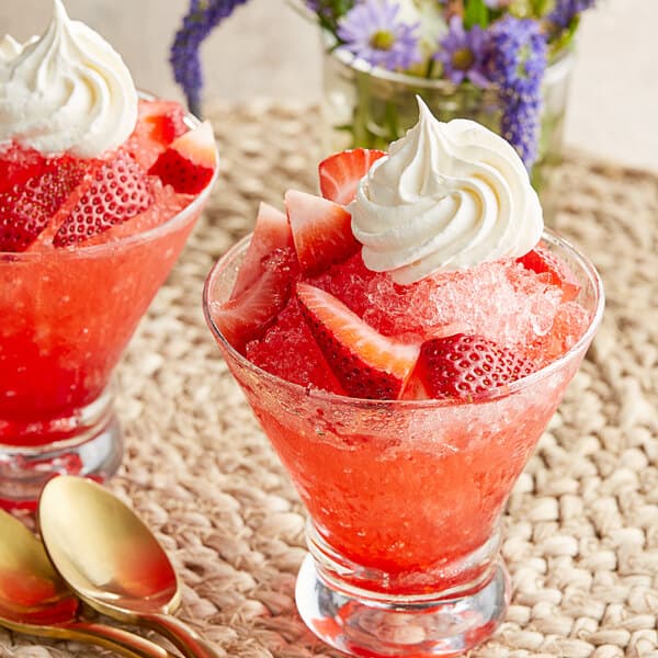 Two glasses with strawberries and whipped cream on top with a spoon in one glass.