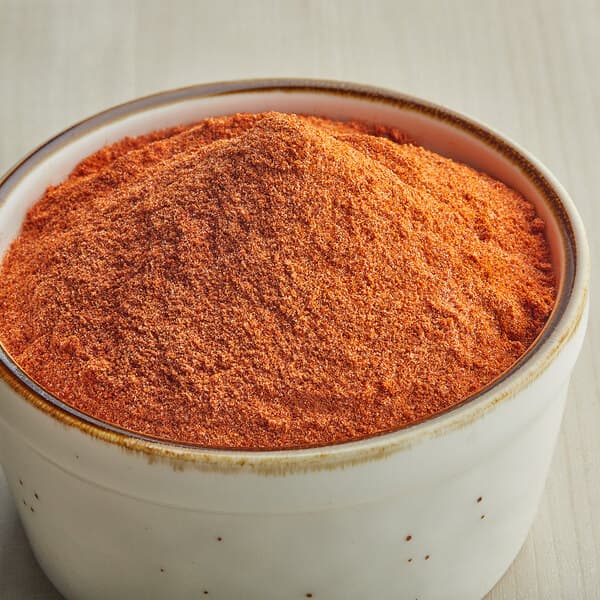 A bowl of Carnival King Smokehouse Popcorn Seasoning, a red powder.