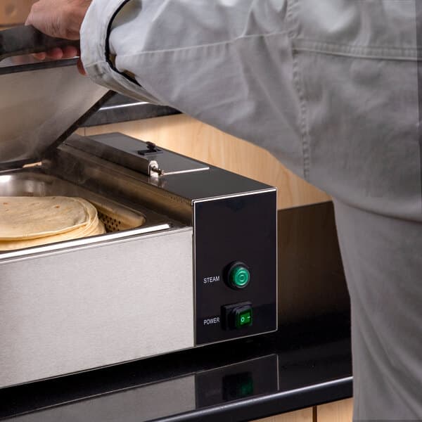 A person using a Carnival King countertop food warmer to cook tortillas.