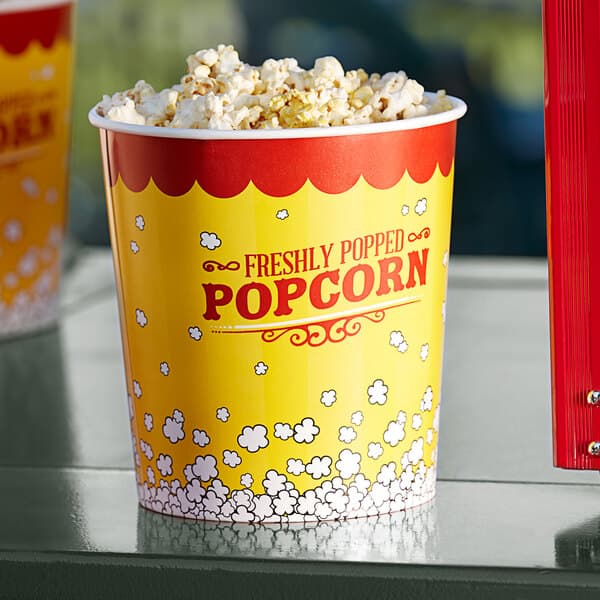 A yellow Carnival King popcorn bucket filled with popcorn on a table.