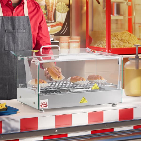 A person in a red apron using a Carnival King hot food display case to serve hot dogs.