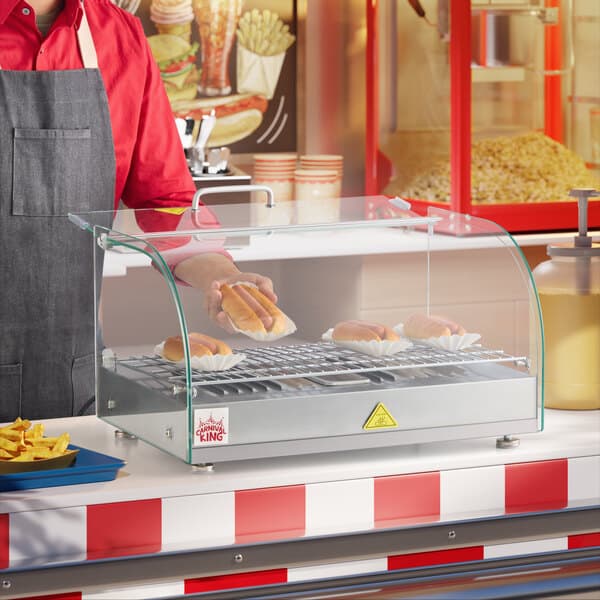 A man serving hot dogs from a Carnival King countertop hot food display case.