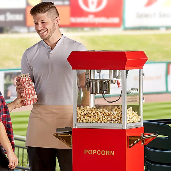 A man standing next to a Carnival King commercial popcorn machine with a bag of popcorn.